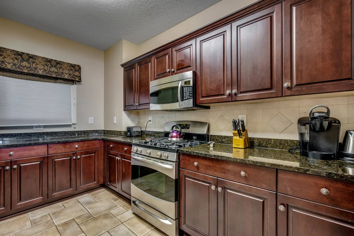 A spacious, modern kitchen featuring granite countertops, stainless steel appliances, dark wood cabinetry, and a kettle on the stove. A coffee maker sits ready for use, hinting at lively breakfasts and coffee breaks. The overall atmosphere is both inviting and functional, radiating a sense of warmth perfect for gathering and cooking together.