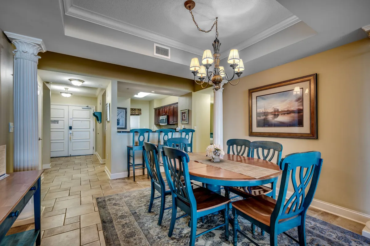 A warm, welcoming dining area with a substantial dining table, a sparkling chandelier above, framed artwork on the walls, and an inviting entrance. The scene projects an ambience ideal for group meals and festive celebrations.