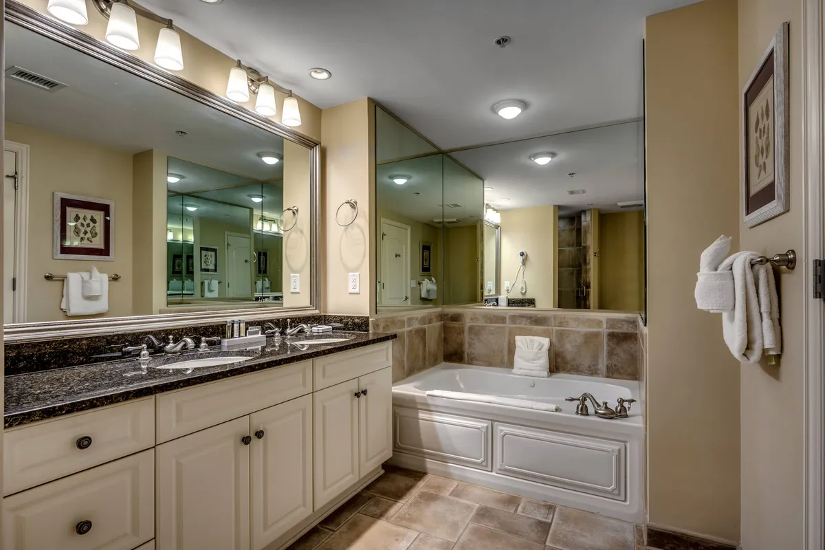 A luxurious bathroom showcasing a sleek soaking tub, a spacious double sink vanity with granite countertops, and a mirrored wall. The space is flooded with soft light, enhancing the tranquil mood and spa-like ambiance.
