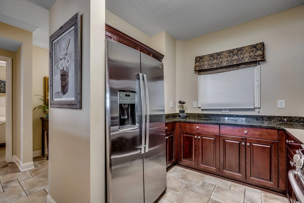 A close-up view of the kitchen area, highlighting a stainless steel refrigerator, granite countertop, wooden cabinets, and tasteful decorative artwork. The setting feels inviting and homey, encouraging family cooking and shared traditions.