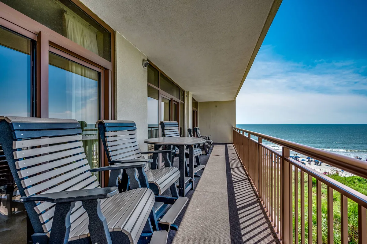 A covered balcony with comfortable chairs and a direct, unobstructed ocean view framed by a simple railing. The setting glows in natural light, inviting moments of quiet reflection or social gatherings with a stunning Atlantic backdrop.