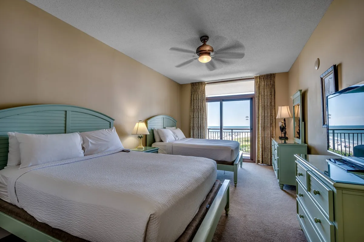 A guest bedroom with two double beds dressed in crisp white linens and light green accents, complemented by a large window that frames a beautiful ocean view. Comfortable furniture and a serene color scheme create an inviting, restful environment.