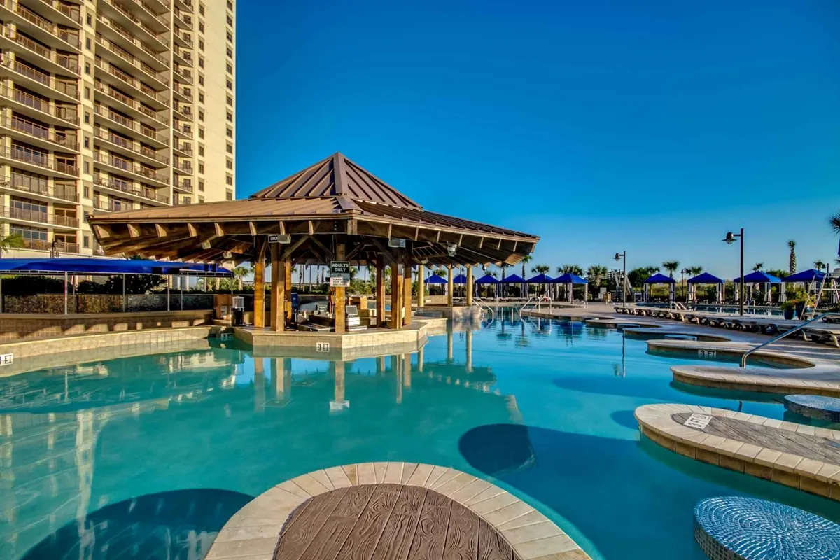 A focused look at a stylish pool area with a pavilion, sun loungers, and a tranquil sky overhead. Guests are seen relaxing, socializing, and enjoying poolside cocktails, suggesting both active fun and relaxation. The setting highlights the inviting atmosphere of the resort's outdoor spaces.